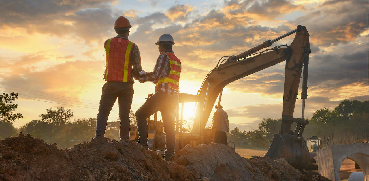 Engineers at a dig site with excavator in the background over a sunrise