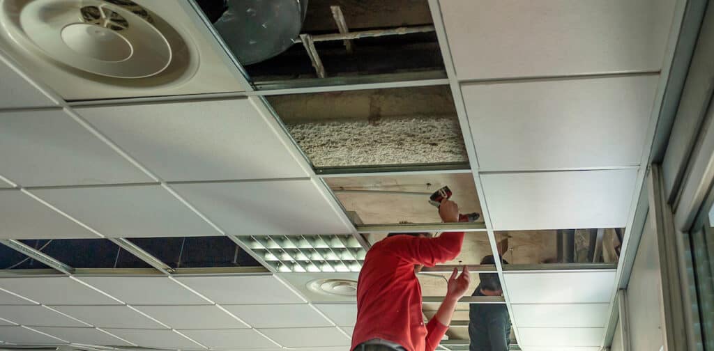 Construction workers assemble a suspended ceiling with drywall and fixing the drywall to the ceiling metal frame.