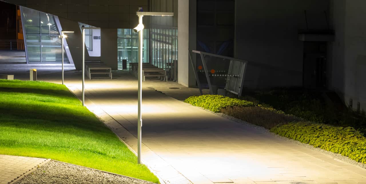 A nighttime photo of an empty campus sidewalk with cameras and lighting