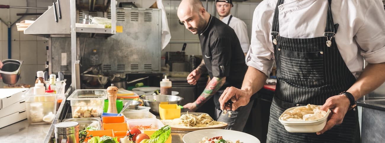 Chefs in a commercial kitchen prepare dishes.