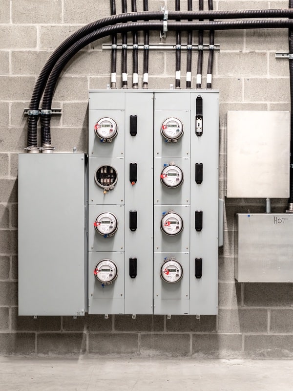 Electrical room with multiple smart meters, cabinets, wiring and fire extinguisher.