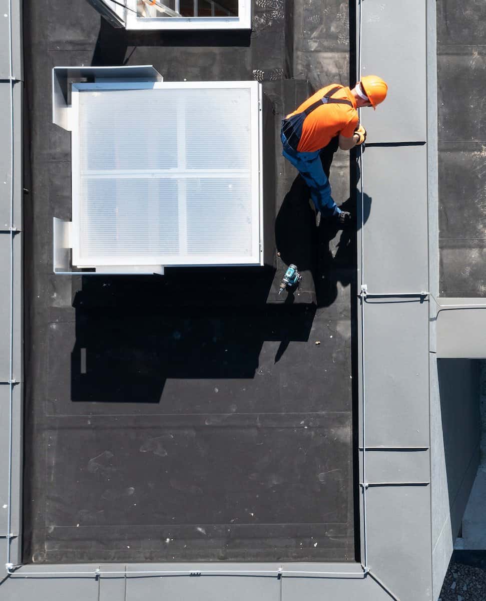 A worker installs a lightning rod atop a building roof to ground lightning strikes.