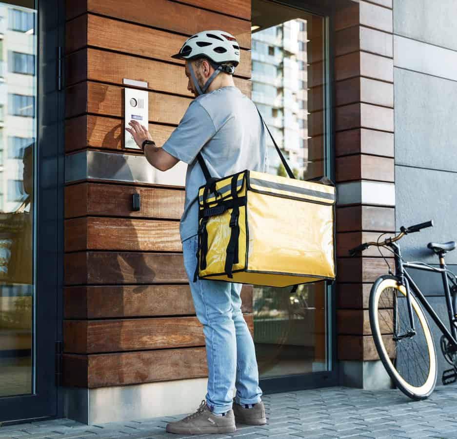 A food delivery driver uses an intercom outside an apartment building.